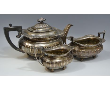 A George V silver three piece half fluted boat shaped tea service, comprising teapot, milk jug and sugar basin, hinged domed 