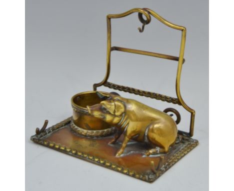 An early 20th century brass novelty combination pocket watch stand and inkwell, as a pig seated beside a trough, rectangular 