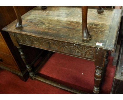 An antique joined oak plank top side table, having floral relief carved frieze and raised on ring turned supports, united by 