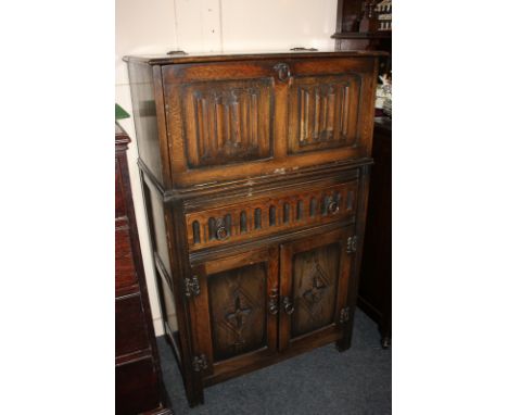 A carved oak drinks cabinet with metamorphic pull-out top revealing mirror lined interior with glass shelf, drawer and cupboa