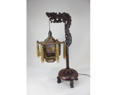 A Chinese carved hardwood table lamp modelled as a dragon , supporting a light fitting, with lantern style shade, on circular