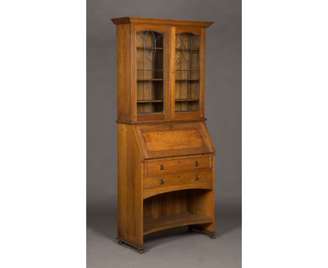 An Edwardian Arts and Crafts oak bureau bookcase, the top fitted with a pair of leaded glass doors, the base with a panelled 