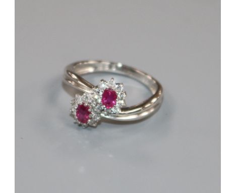 A modern 18ct white gold, ruby and diamond double cluster crossover ring, size M.