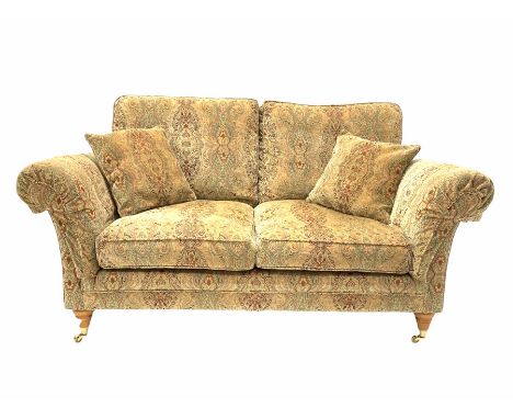 Parker Knoll - two seat sofa, upholstered in golden medallion fabric, with two small cushions and supported by two brass cast