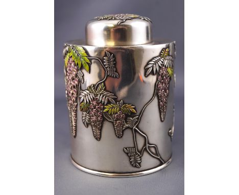 A Japanese white metal round form tea canister, decorated with polychrome enamel cameo wisteria blossoms and a bird in flight
