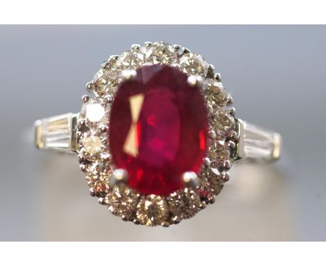 A white metal cluster ring, set with an oval faceted cut composite ruby (glass filled) and surrounded by round brilliant cut 