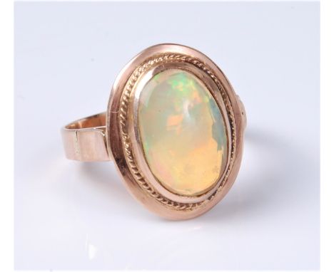 An opal ring, the oval cabochon approx. 12.8 x 9.1mm, in a stepped rubover mount with ropetwist border, to supported shoulder