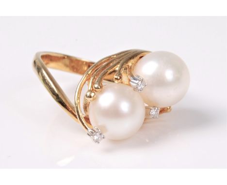 A pearl and diamond ring, the two asymetrically set pearls, each approx. 8.5mm diameter, held in reeds of yellow precious met