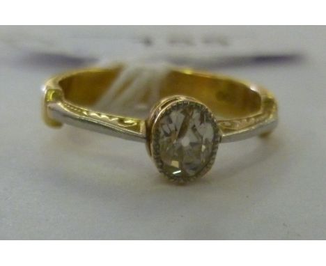 A bi-coloured metal ring, set with a single oval shaped diamond, flanked by C-scrolled ornament          11