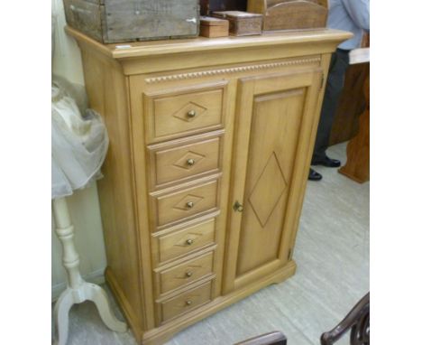 A modern light oak tallboy with six drawers, beside a panelled door, enclosing two height adjustable shelves, raised on brack