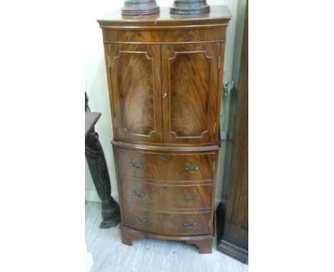 A modern mahogany finished bow front cocktail cabinet, having a pair of doors, enclosing two shelves, over a single door, rai