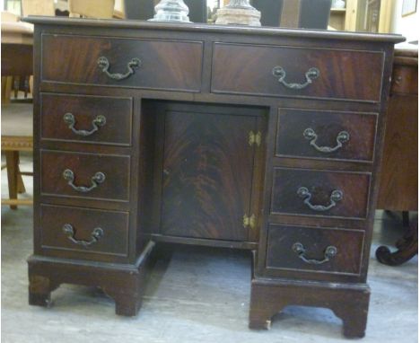 A modern Georgian inspired mahogany finished kneehole desk, having a faux brown hide scriber, over a door and eight drawers, 