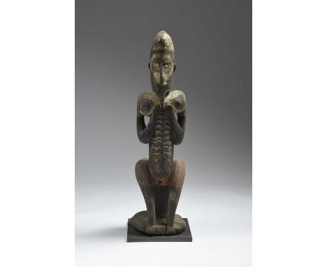 A Middle Sepik River female ancestor figurePapua New Guineaseated on a mask support and with inset cowrie shell eyes, pierced