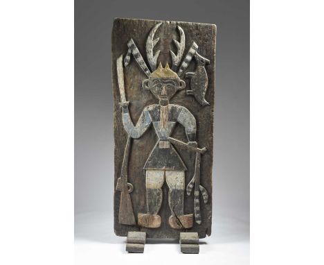 A Paiwan house panel Taiwanrelief carved a standing warrior wearing a horned headdress with feathers and holding a long knife