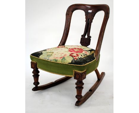 A LATE VICTORIAN LOW ROCKING CHAIR with pierced and carved back and overstuffed upholstered tapestry seat standing on taperin