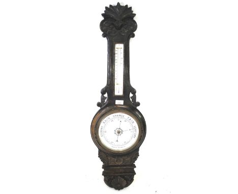 An ebonised aneroid banjo barometer. With carved decoration above a Fahrenheit and centigrade thermometer. The banjo above a 