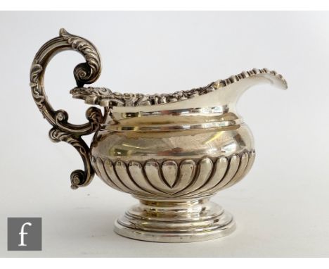 A George III hallmarked silver melon shaped pedestal cream jug terminating in acanthus capped scroll handle, Sheffield 1819, 