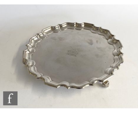 A hallmarked silver circular salver raised on four scroll feet with central engraved crest within pie crust border, diameter 