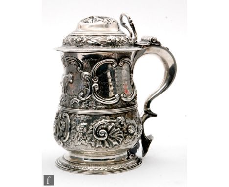 A George II hallmarked silver tankard and cover later embossed with foliate embossed and engraved decoration around a central