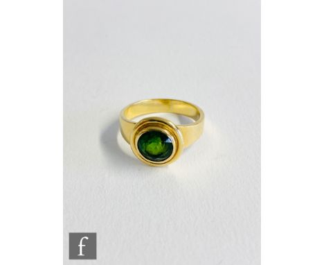 An 18ct single stone green tourmaline ring, central circular collar set stone within a plain gold border and tapering shoulde