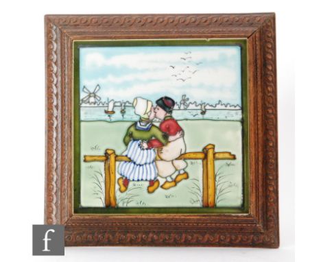 A framed 8in tile decorated with a tubelined Dutch scene with a lady and gentleman kissing whilst looking out to sea with a w