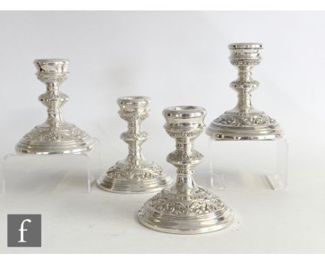 A composed set of four hallmarked silver squat candlesticks with part embossed foliate decoration to circular stepped bases, 