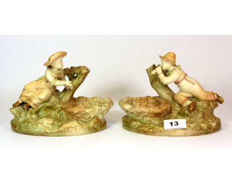 A pair of Royal Worcester blush ivory porcelain figures designed by James Hadley modelled as a boy and a girl leaning against