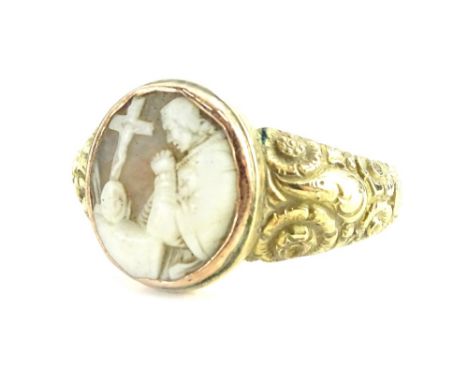 A cameo dress ring, the cameo depicting a man praying, in gold frame, with floral scroll design shoulders, yellow metal unmar