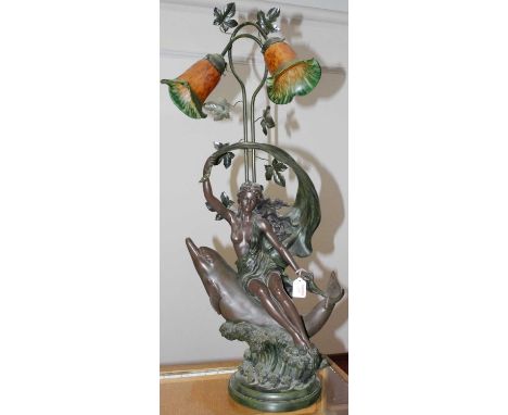 An Art Nouveau style bronzed composite twin branch table lamp, in the form of a lady seated on a dolphin, h.99cm