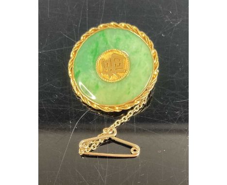 A Chinese yellow metal and jade disc brooch, the centre set with a Chinese symbol, with safety chain, steel pin, tests as app