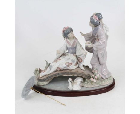 A Lladro porcelain figure of two geishas beside on a bridge with a swan below, with a parasol, on baize lined wooden plinth, 