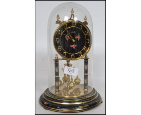 A 20th century anniversary clock complete in the glass dome with brass swing weights having black dial with flowers