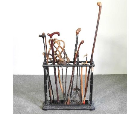 A cast iron six division stick stand, 61cm wide, containing a collection of novelty walking sticks and riding crops