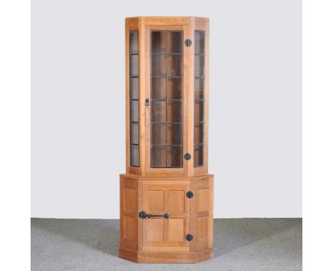 Robert 'Mouseman' Thompson, of Kilburn, a light oak standing corner cabinet, enclosed by a lead glazed door, over a panelled 