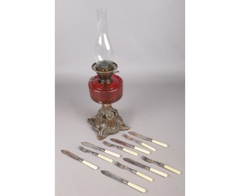A Victorian cranberry glass oil lamp along with a collection of fish knives and forks.  
