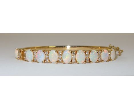 An 18ct opal and diamond bangle the oval white opals with nice colour play are interspaced with sets of triple diamonds, to a