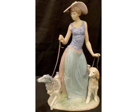 A Lladro figure, Elegant Promenade, as a fashionable lady in wide brimmed hat walking a pair of dogs, number 5802 J-22 K, 39c