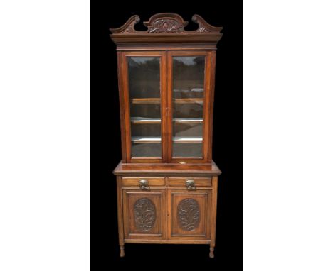 An Edwardian walnut bookcase on cupboard with twin swan necked arched pediment above a pair of glazed doors enclosing adjusta