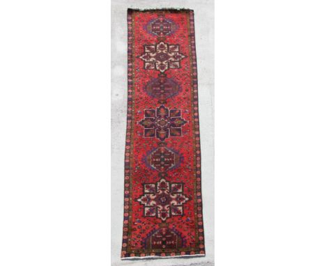 A Persian hand knotted runner with repeat star design within floral borders, on a red ground, 380 by 90cms (419).
