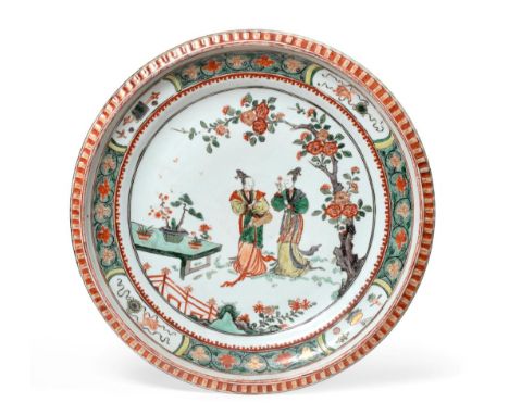 A Chinese Porcelain Charger, Kangxi, painted in famille verte enamels with figures in a fenced garden within a foliate border