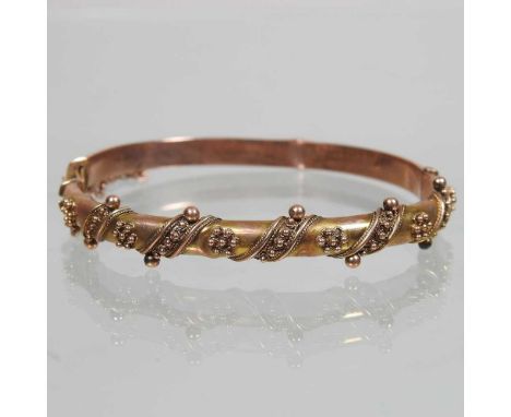 An early 20th century 9 carat gold bangle, of hinged design, with applied decoration and safety chain, 7.3g, 6cm wide