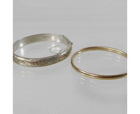 A 9 carat gold bangle, of plain hinged design, 6.2g, 6cm wide, together with a hallmarked silver bangle, 16.7g, 7cm wide (2)