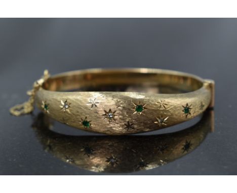 A 9ct gold hinged bangle having diamond and emerald chip decoration in star burst settings on brushed finish,  approx 16.2g