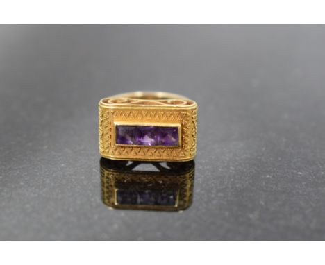 A yellow metal (thought to be gold) and amethyst dress ring, having a linear arrangement of three princess cut amethysts, wit