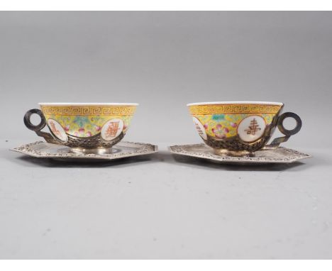 A pair of engraved and chased white metal mounted Chinese polychrome enamel decorated cups and saucers 
