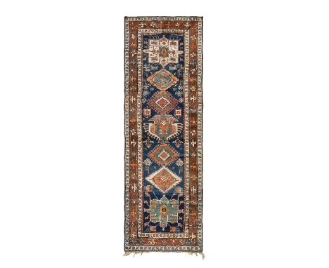 Karabagh Runner, circa 1920The abrashed indigo field with a column of terracotta ivory and mint green medallions surrounded b