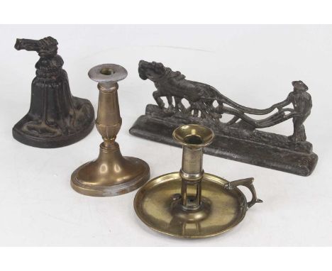 A black painted cast iron door stop in the form of a bell, together with a brass candlestick in the 18th century style, brass