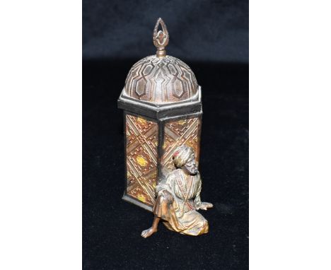 A BERGMANN BRONZE STYLE PAINTED METAL GROUP  modelled as an Arabian gentleman seated leaning against a small tower, the lid o