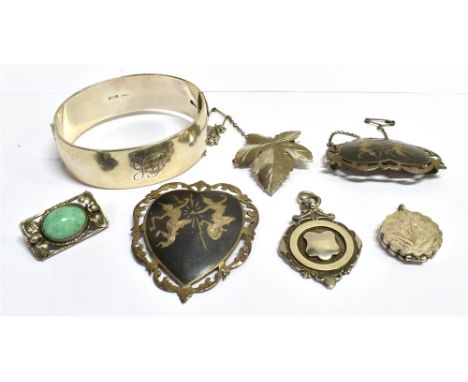A COLLECTION OF JEWELLERY Comprising a silver half patterned bangle; three silver brooches; a marked silver floral locket; an
