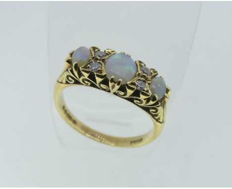 A graduated three stone opal Ring, each set with two diamonds between, in a scroll gallery, the shank marked 750, Size O½. 